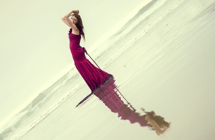 Woman standing on beach with arms over head as if holding off the world.